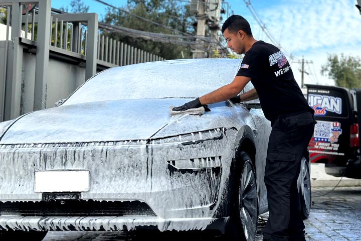 Una persona del equipo seca un SUV cubierto de espuma en plena calle, con la van detrás